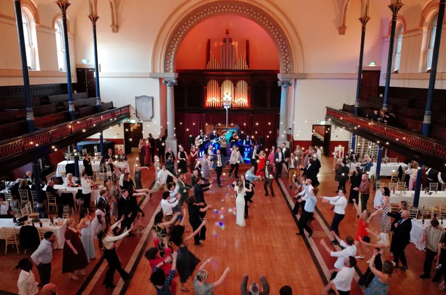 Wedding guests dancing a ceilidh in a grand hall with an organ